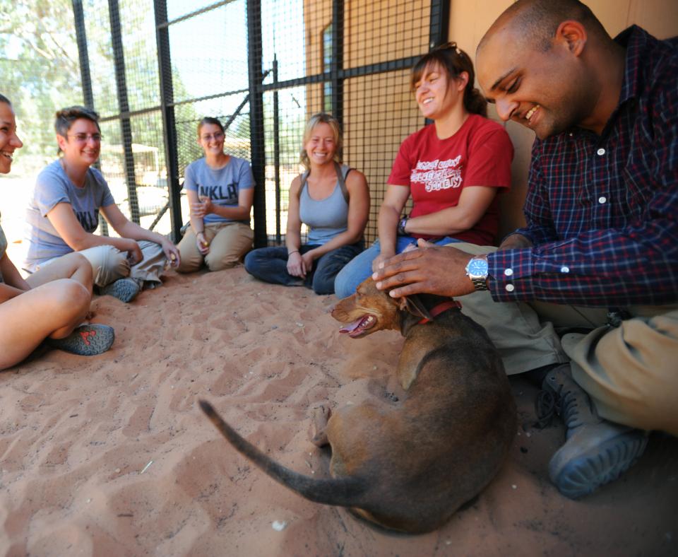 Group of smiling people sitting with a dog in sandy area in Utah desert